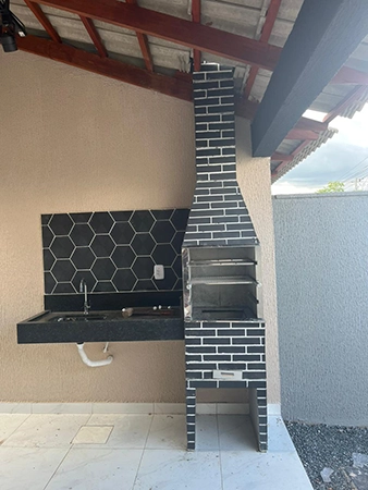 imagem de uma churrasqueira com tijolos pretos, com uma pia preta ao lado
