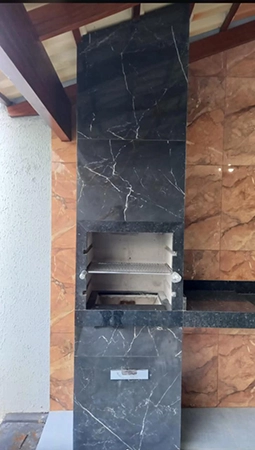 imagem de uma churrasqueira com azulejos pretos, com uma pia preta ao lado